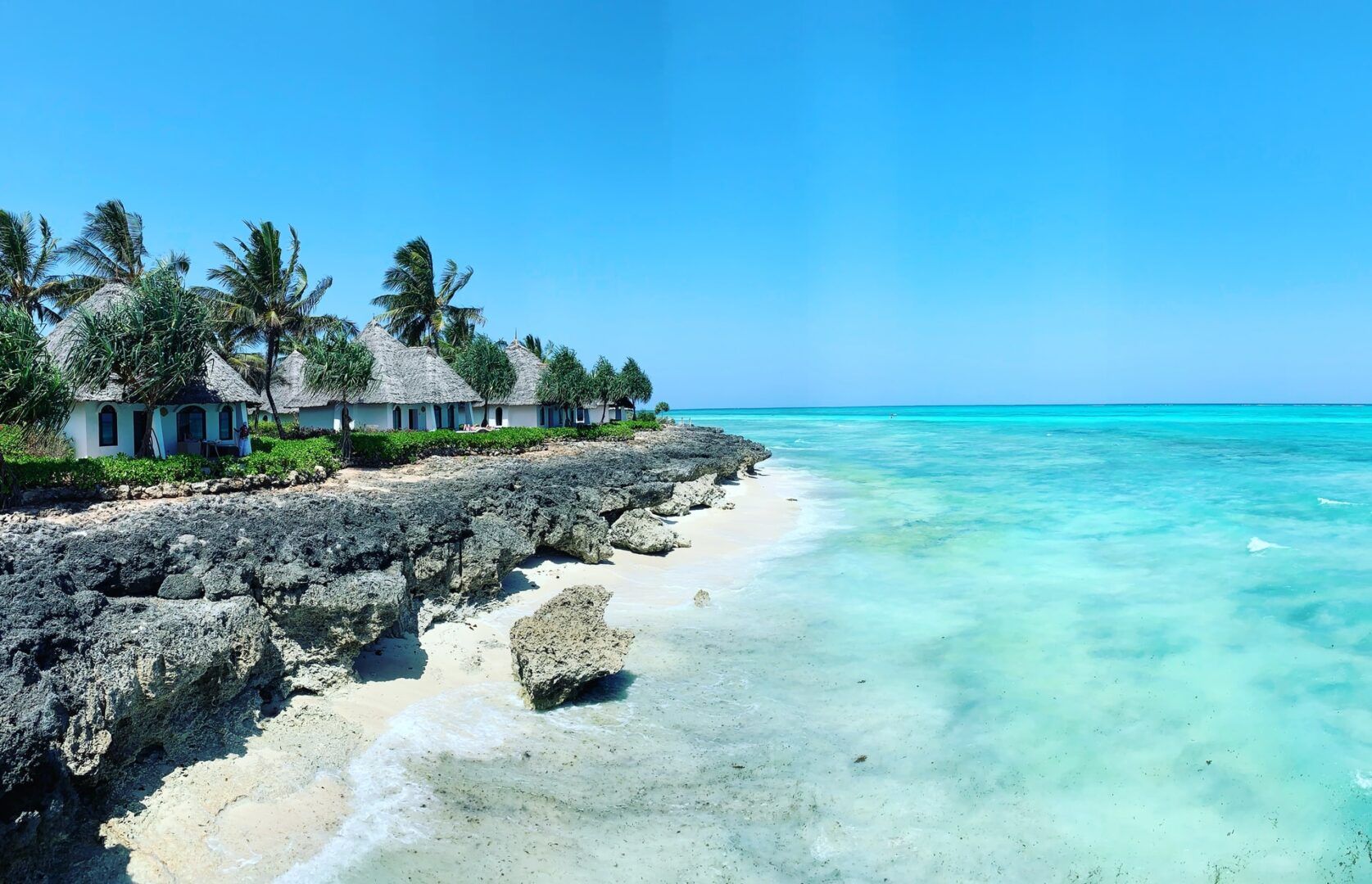 Rocky Zanzibar shoreline with thatched coastal cottages and clear ocean water
