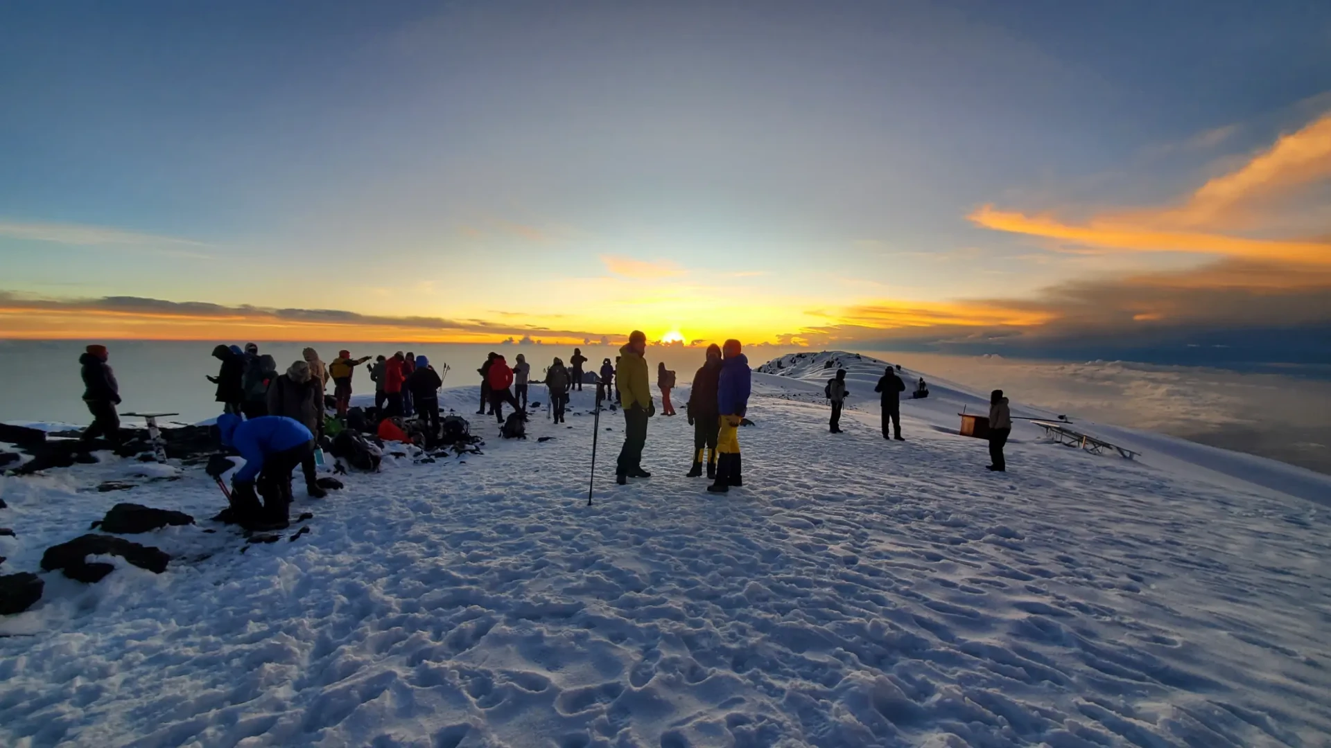 Climbers resting on Mount Kilimanjaro's snowy summit ridge at sunrise