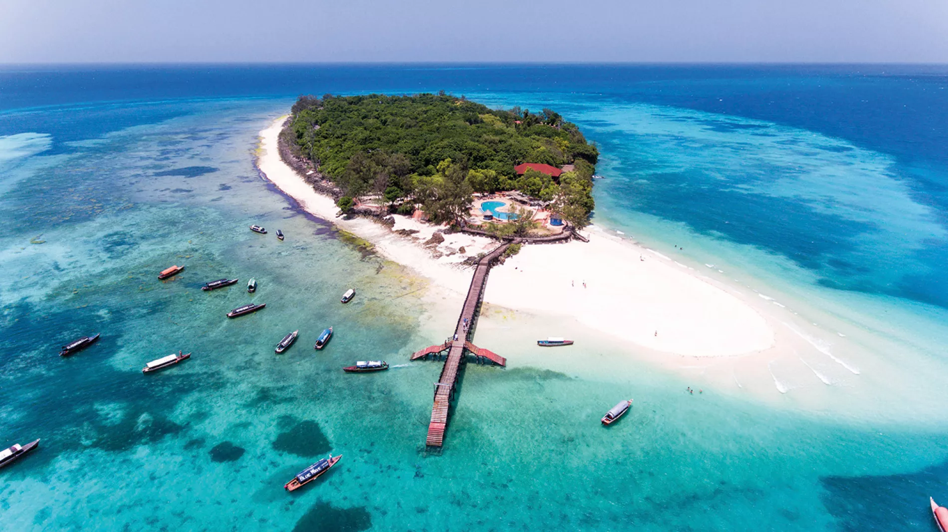 Aerial view of a small forested island and white sand surrounded by turquoise water in Zanzibar