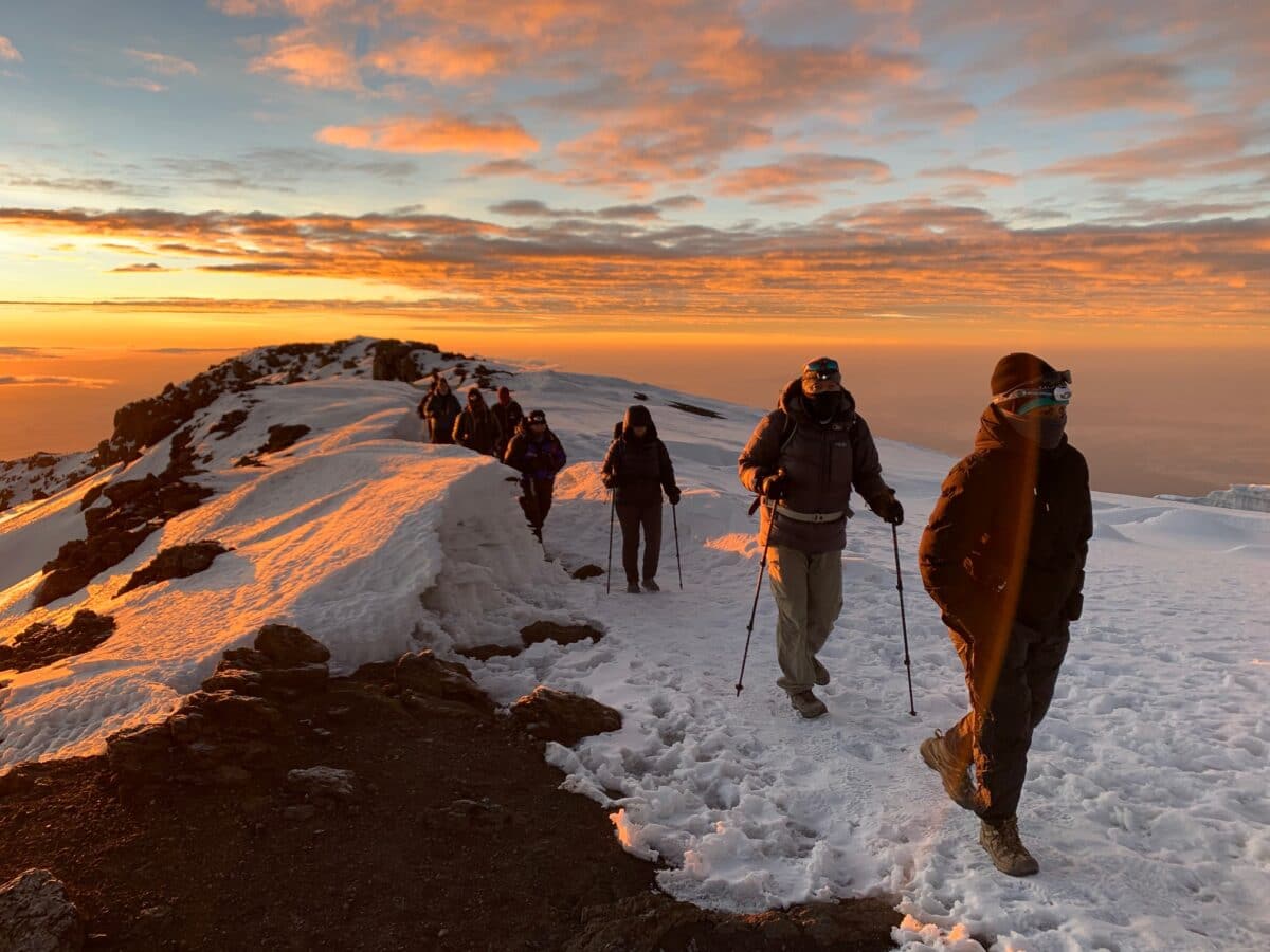 Trekkers climbing Mount Kilimanjaro's snowy summit slopes at sunrise