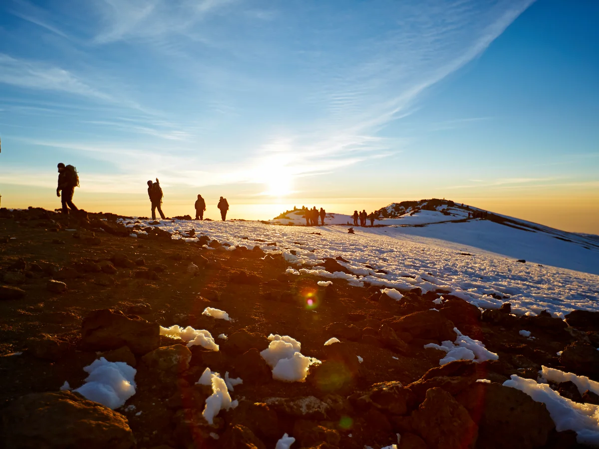 Climbers walking across snow on Mount Kilimanjaro at sunrise